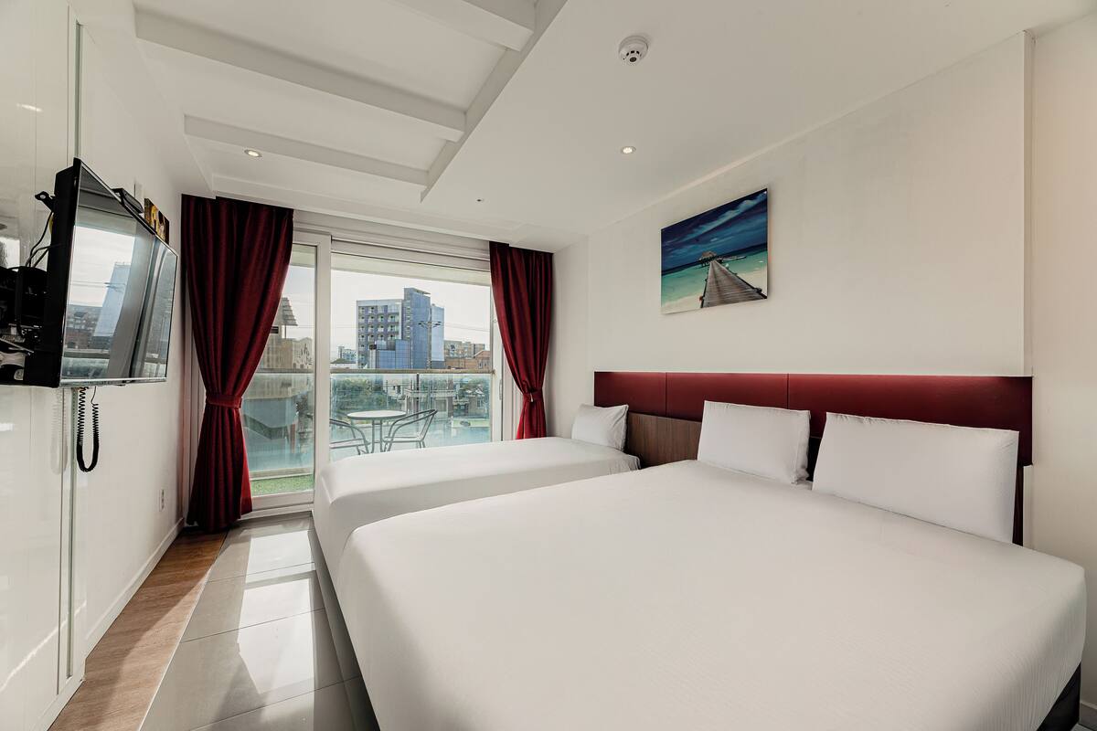 Ein Hotelzimmer mit zwei Betten, einem Fernseher und einem Balkon mit Blick auf die Stadt.