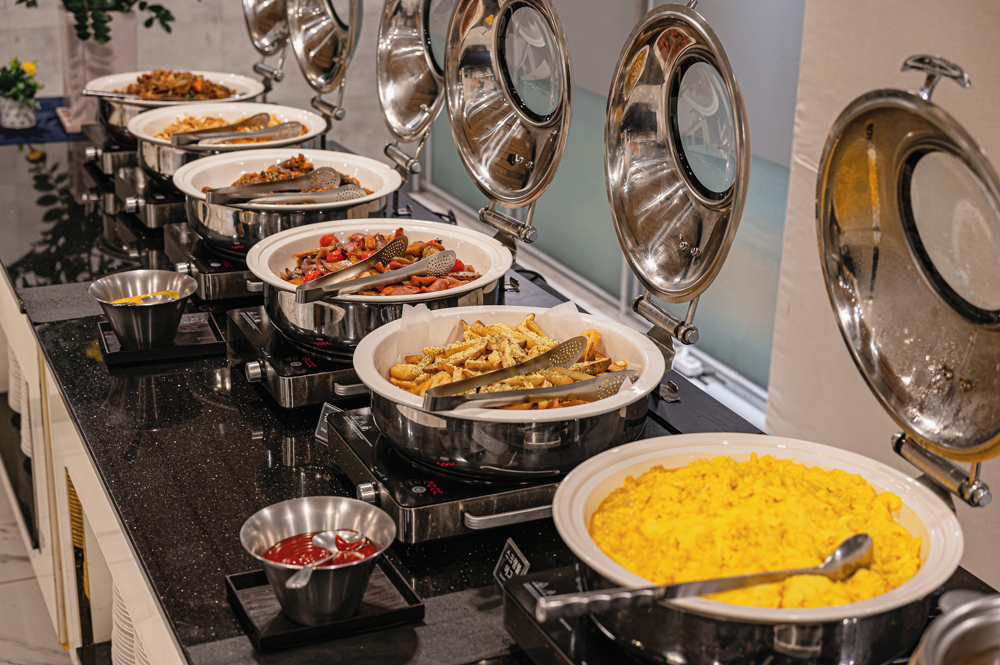 A buffet with various dishes in metal serving dishes, arranged on a black countertop.