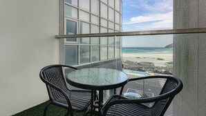 Un balcon avec une table et des chaises en verre, donnant sur une plage et l’océan.