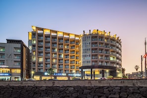 A multi-story hotel with balconies, a curved section, and a stone wall in the foreground.