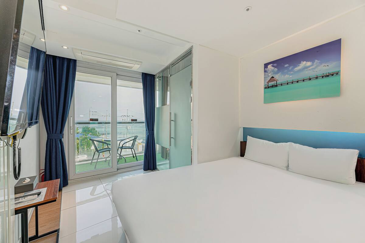 Ein Hotelzimmer mit einem großen Bett, einem Schreibtisch mit Telefon und einem Balkon mit Meerblick.