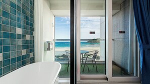 Une salle de bain avec une baignoire et une vue sur la plage, accessible par une porte vitrée.