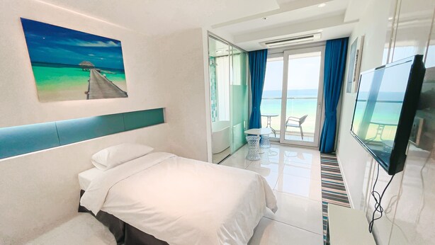 Une chambre d’hôtel avec un lit, une télévision, un tableau représentant une plage et un balcon donnant sur la mer.