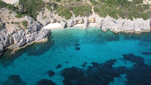An aerial view of a coastal area with rocky cliffs, clear turquoise waters, and a sandy beach. - Villa Alkionis in Kefalonia (Skala Kefalonia)