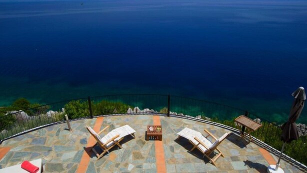 A terrace with two lounge chairs and a table, overlooking a clear blue sea. - Villa Alkionis in Kefalonia (Skala Kefalonia)