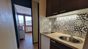 A kitchen with patterned tiles, a sink, and a view of a balcony. - Functional studio on the slopes, renovated, balcony, pet-friendly (La Plagne)