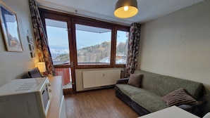 A cozy room with a sofa, a table, and a window offering a view of a snowy landscape. - Functional studio on the slopes, renovated, balcony, pet-friendly (La Plagne)