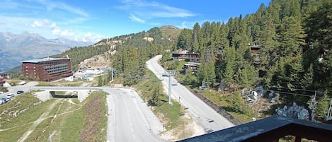 A road winding through a mountainous area with a building on the left and a forested hillside.