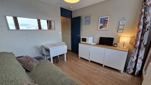 A compact living space with a sofa, a small dining table, a kitchenette, and a view of the outdoors. - Functional studio on the slopes, renovated, balcony, pet-friendly (La Plagne)