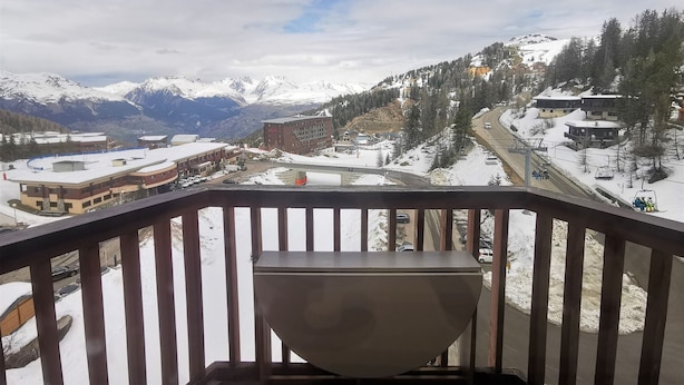 A balcony with a view of a snowy mountain landscape, a road with vehicles, and a building with a ski lift. - Functional studio on the slopes, renovated, balcony, pet-friendly (La Plagne)