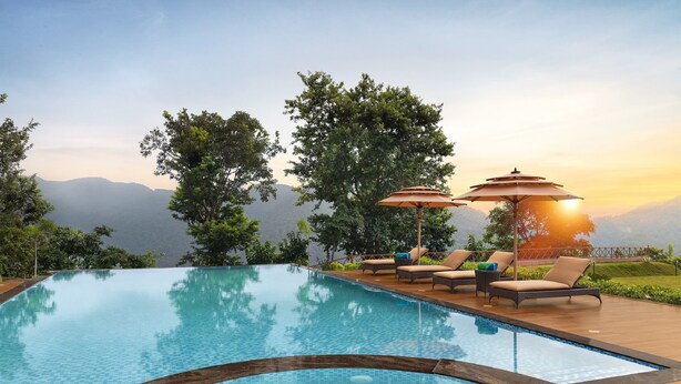 Una piscina con sillas de descanso y sombrillas, rodeada de árboles y vistas a montañas.
