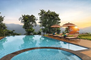 A pool with lounge chairs and umbrellas, surrounded by trees and a view of mountains. - Welcomhotel By ITC Hotels Jim Corbett (Salt)