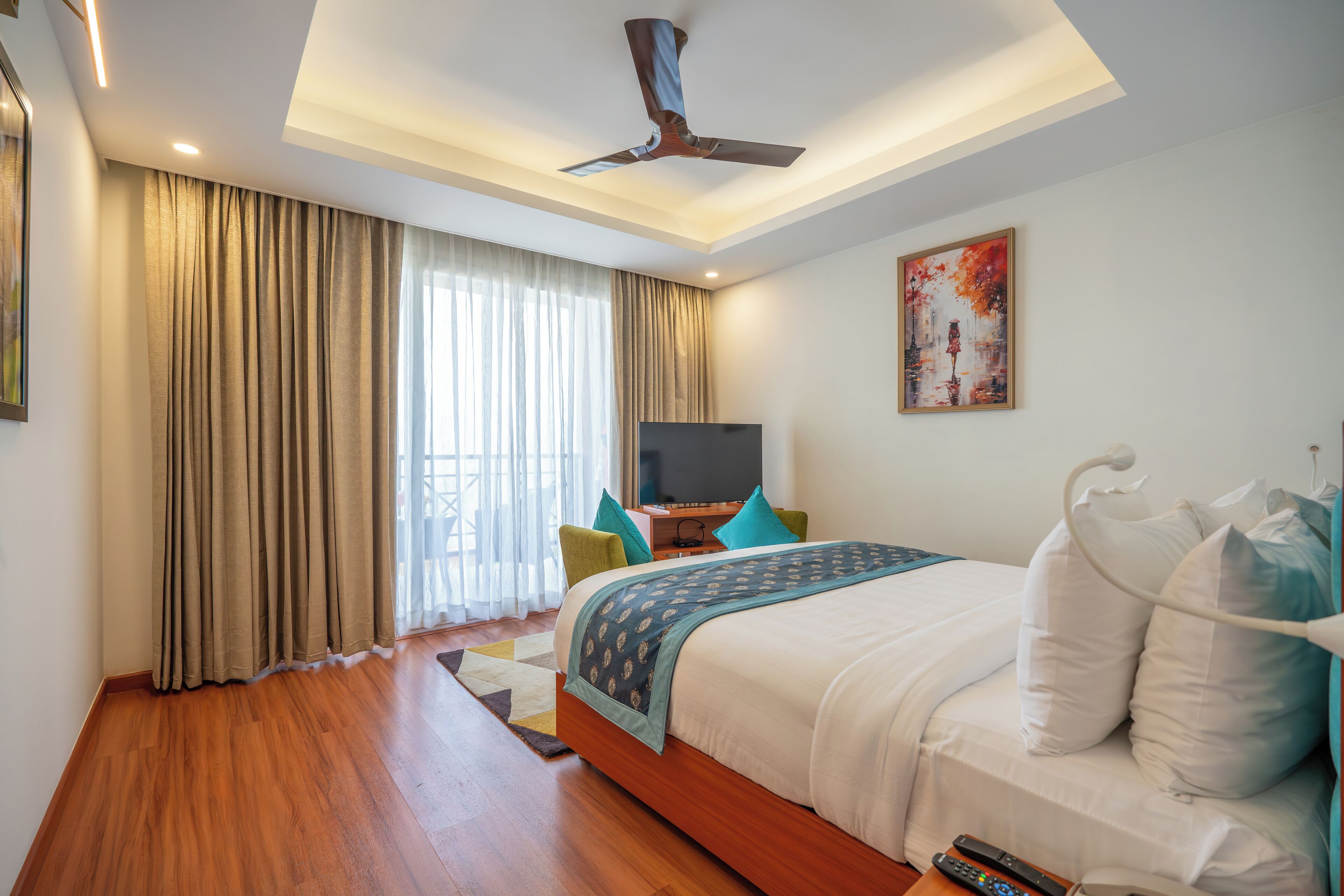 A modern hotel room with a large bed, a ceiling fan, a flat-screen TV, and a painting on the wall.