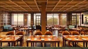 Un comedor amplio con varias mesas y sillas, ventanas grandes que ofrecen vistas a la montaña y un techo de madera.