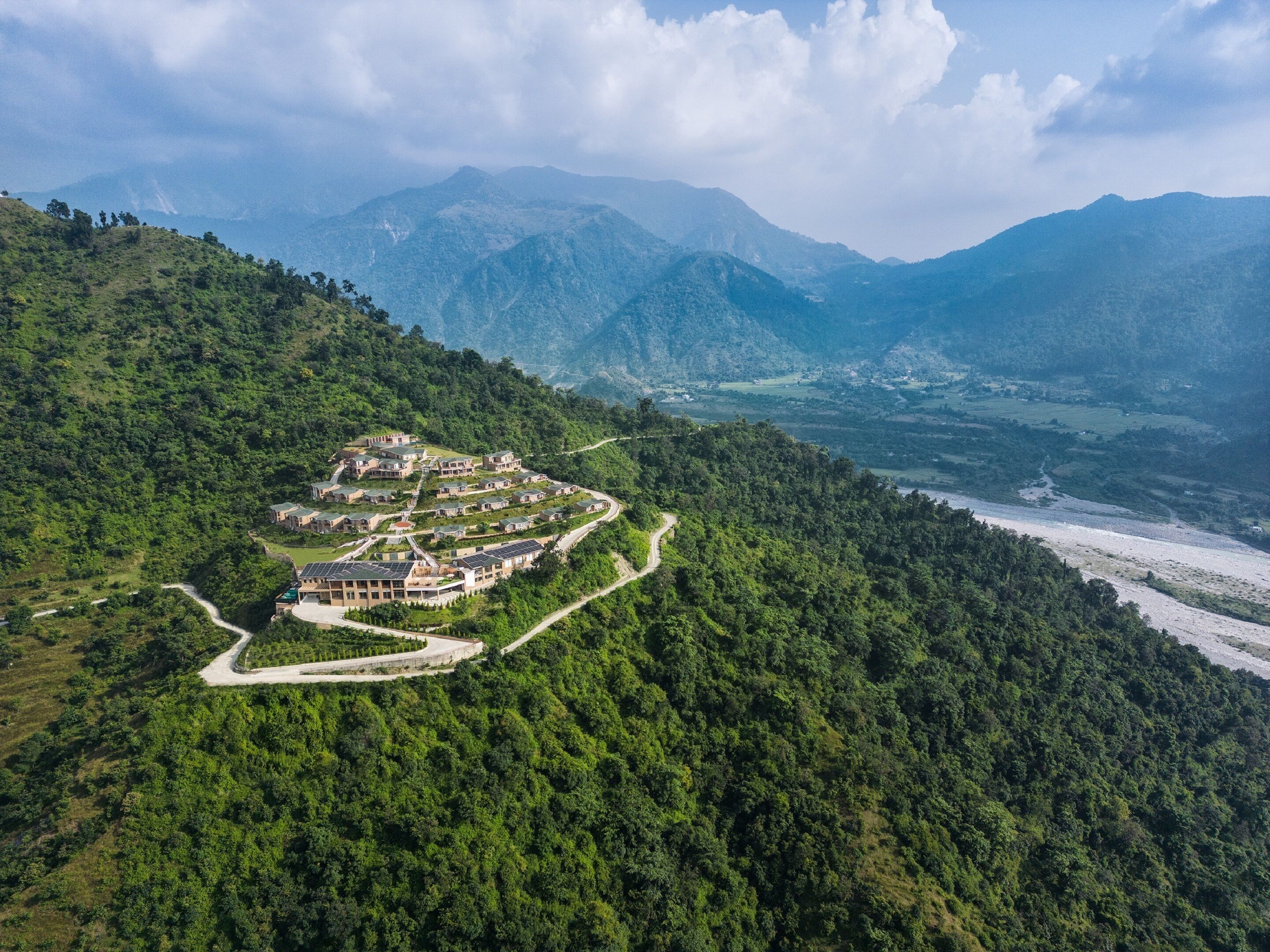 Resort numa encosta com vários edifícios dispostos em semicírculo, rodeado por floresta densa e com vista para um vale.