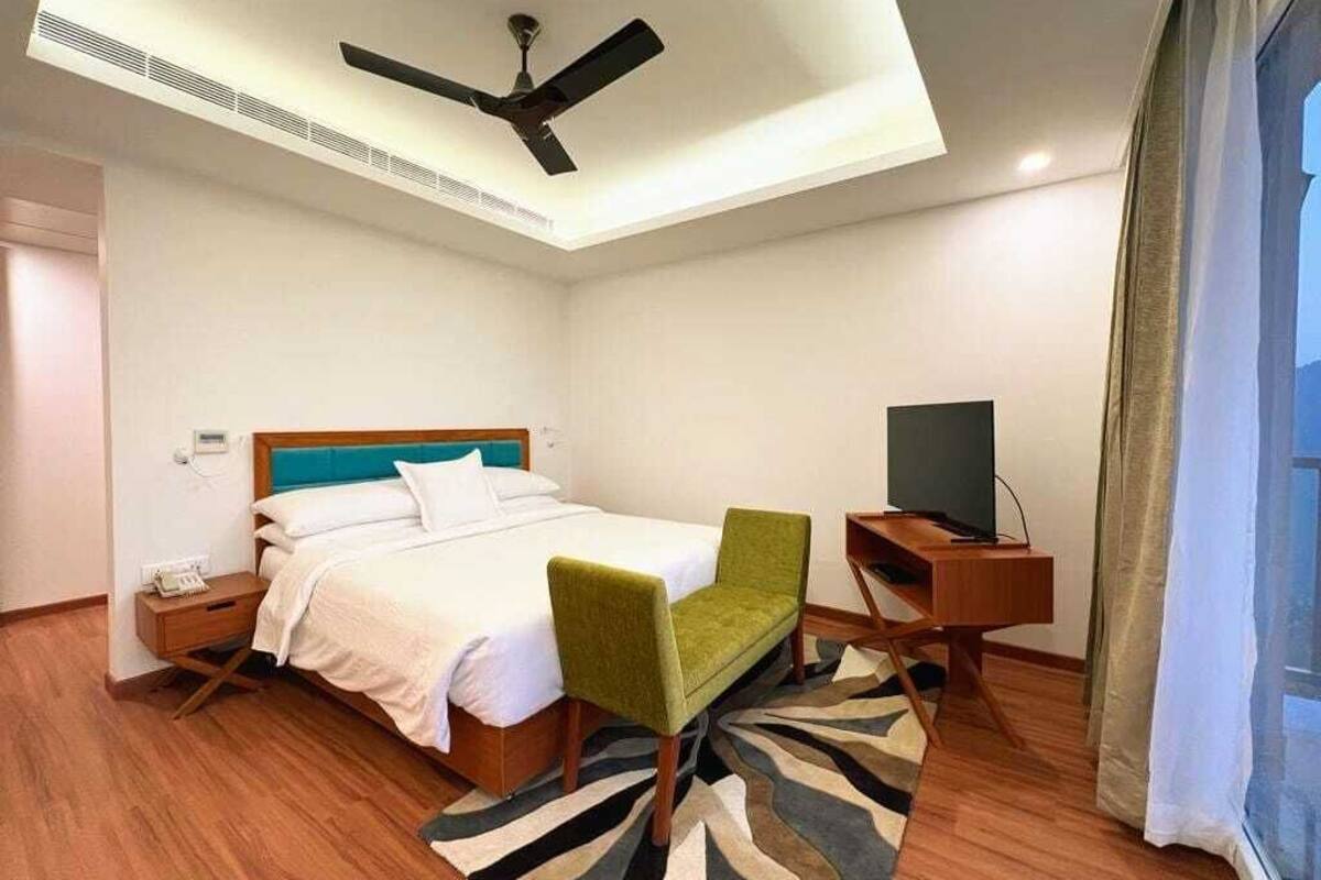 Una habitación de hotel con cama, escritorio, silla, televisor y ventilador de techo.