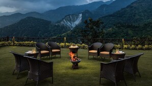 Un patio con mobiliario de mimbre y una chimenea, con vistas a un paisaje montañoso.