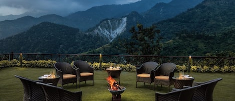 A patio with wicker furniture and a fire pit, overlooking a mountainous landscape.