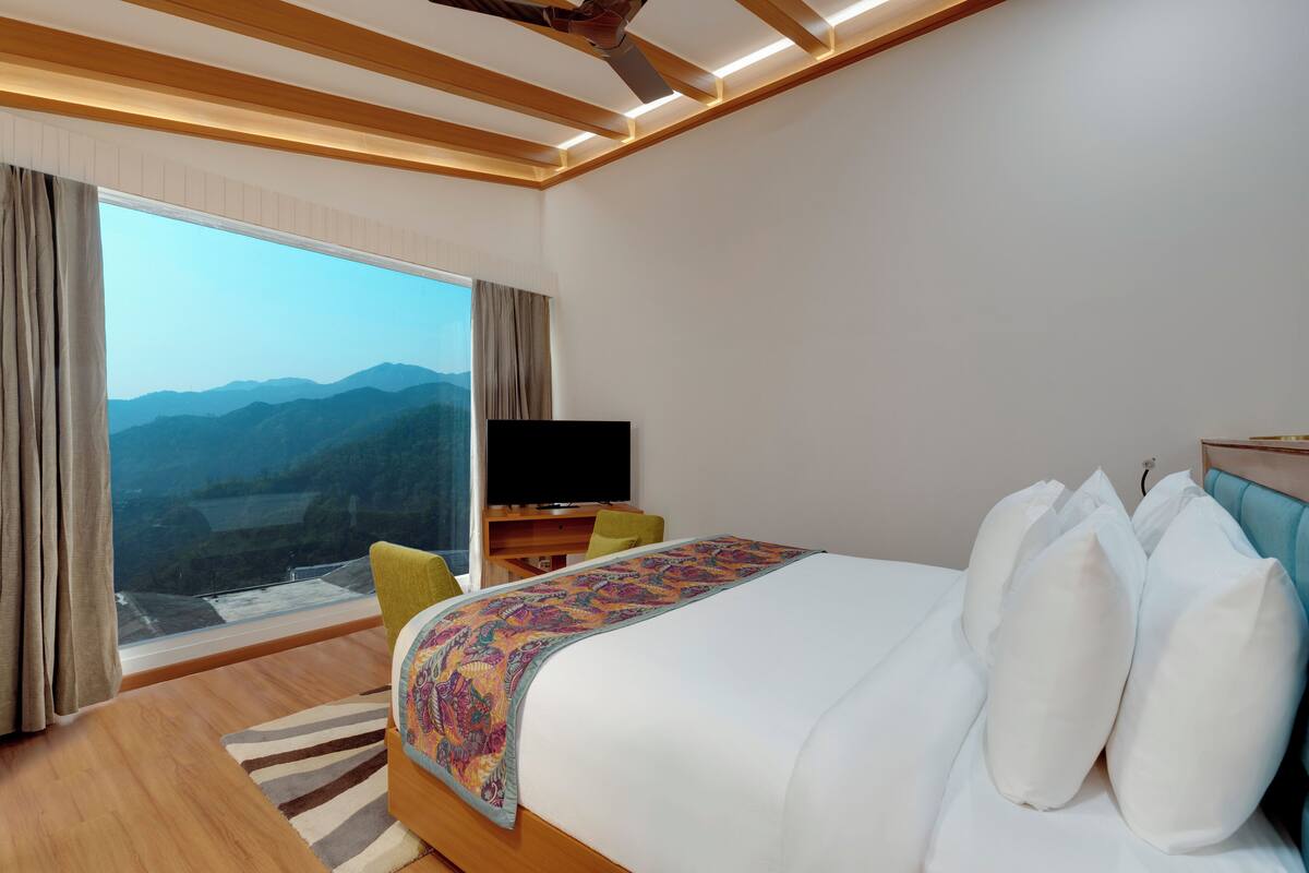 Habitación de hotel con una cama grande, televisión de pantalla plana, escritorio y vistas a las montañas a través de la ventana.