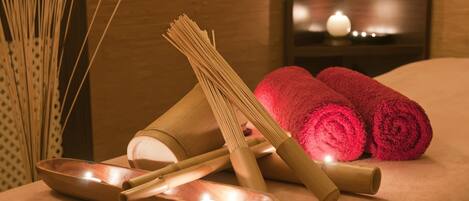 A spa setting with a massage table, rolled towels, and bamboo sticks.