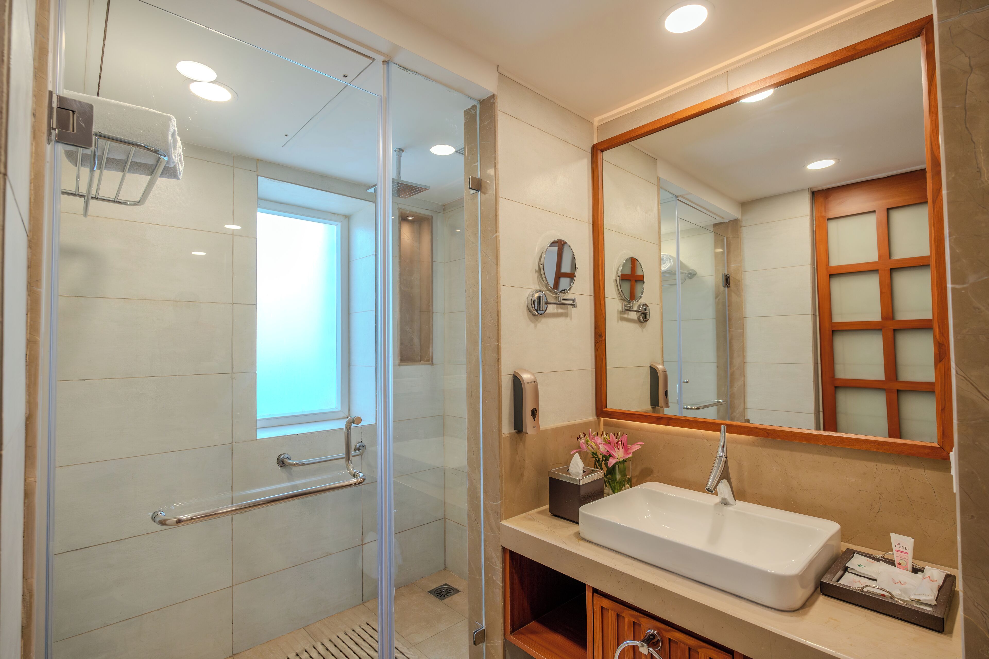 Een moderne badkamer met een douche met glazen wand, een grote spiegel en een wastafel met toiletartikelen.