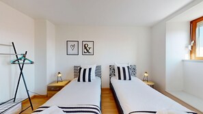 A twin room with two beds, a coat rack, bedside tables, and a window.