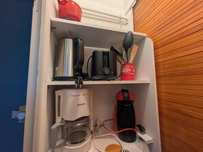A kitchen with a coffee maker, toaster, and kettle on the shelves.