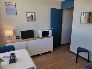 Ein kleines Zimmer mit Fernseher, Mikrowelle, Schreibtisch, Stuhl und einem Tisch mit Pflanze.