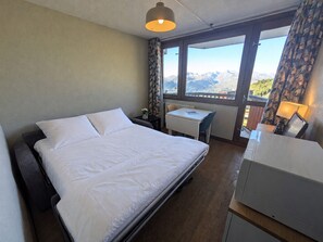 A hotel room with a bed, a desk, and a view of mountains.