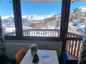 Ein Zimmer mit Blick auf schneebedeckte Berge, ein Tisch mit Pflanze und Broschüre sowie ein Stuhl.