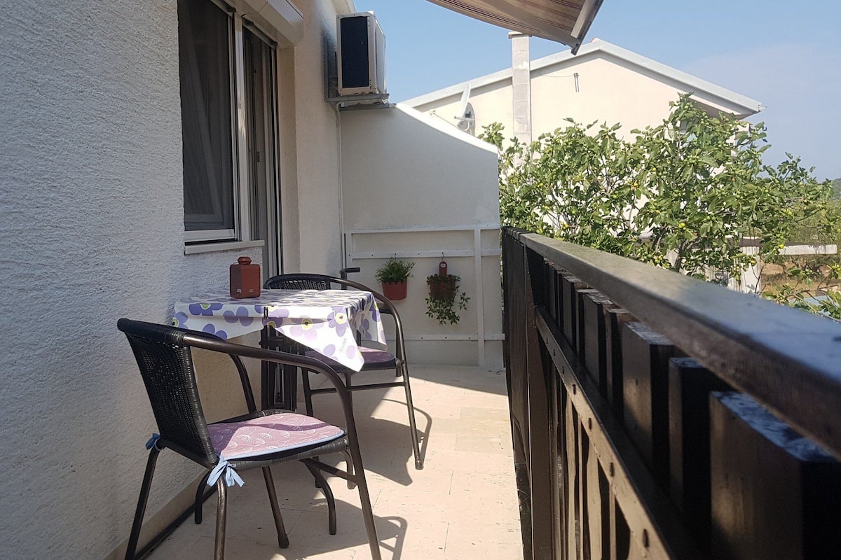 Ein Balkon mit Tisch, Stühlen, einer Topfpflanze und Blick auf ein Gebäude und Bäume.