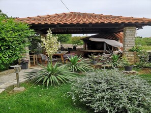 Un área de patio al aire libre con una parrilla de piedra, muebles de madera y plantas en macetas.