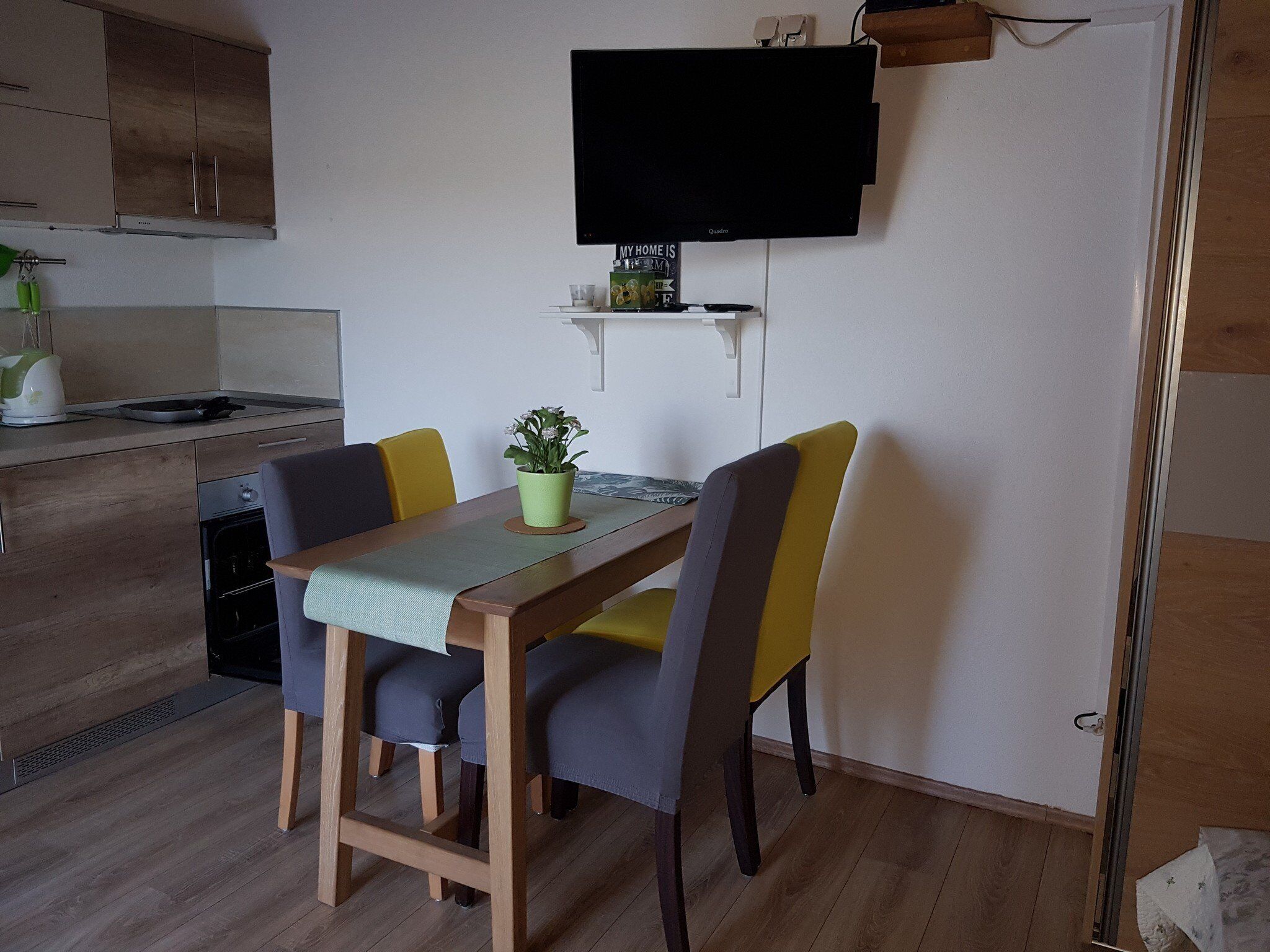 A modern kitchen with wooden cabinets, a built-in oven, and a dining area with a table and chairs.