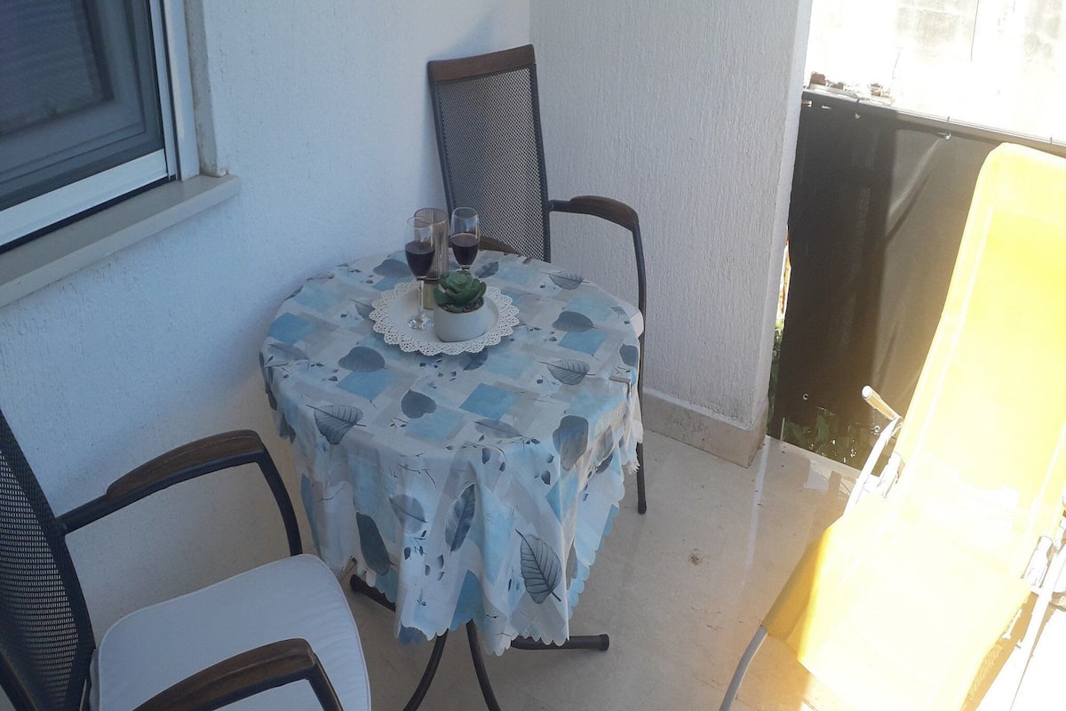 Ein kleiner Tisch im Freien mit Tischdecke, zwei Stühlen und einem Blumentopf.