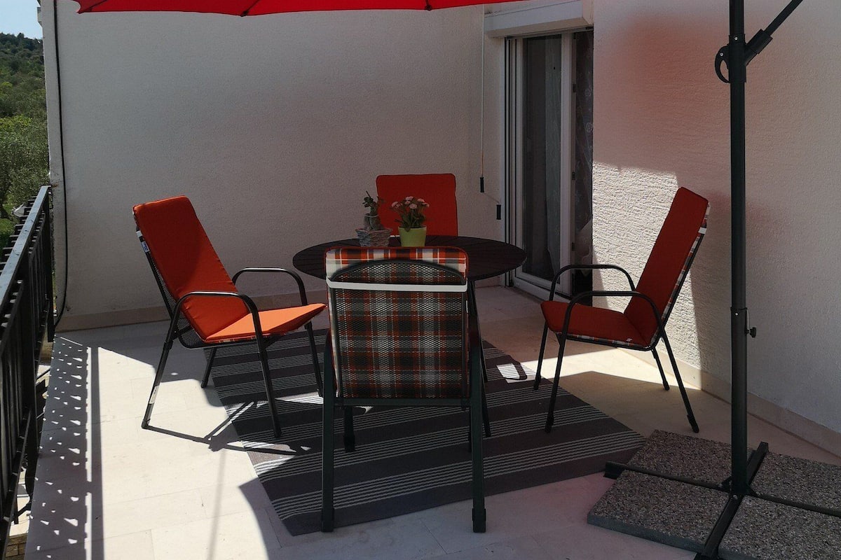 Eine Terrassengruppe im Freien mit Tisch und vier Stühlen, einem roten Sonnenschirm und einem kleinen Topfpflanzen.
