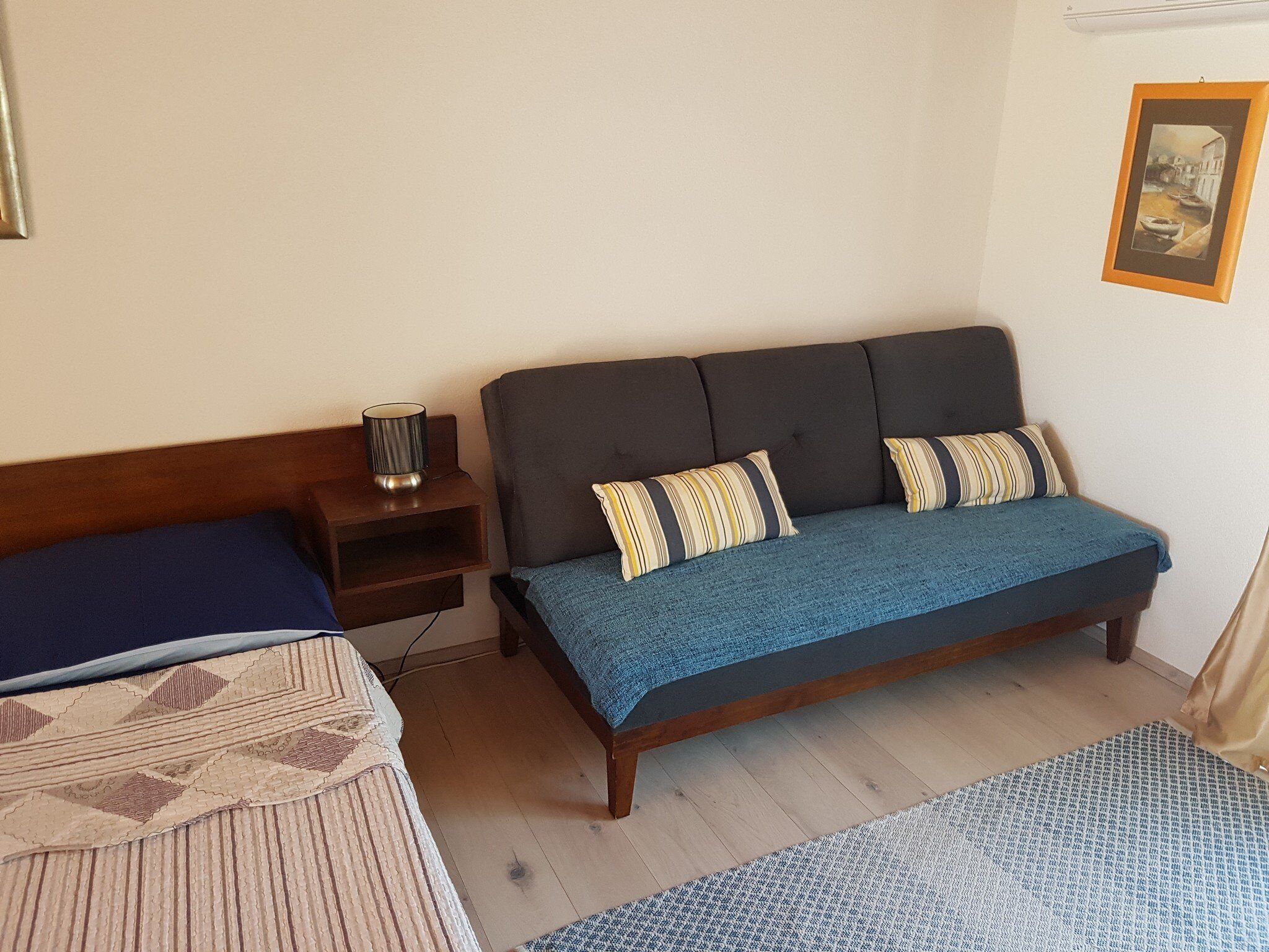 Un dormitorio con cama, mesita de noche con lámpara y un cuadro en la pared.
