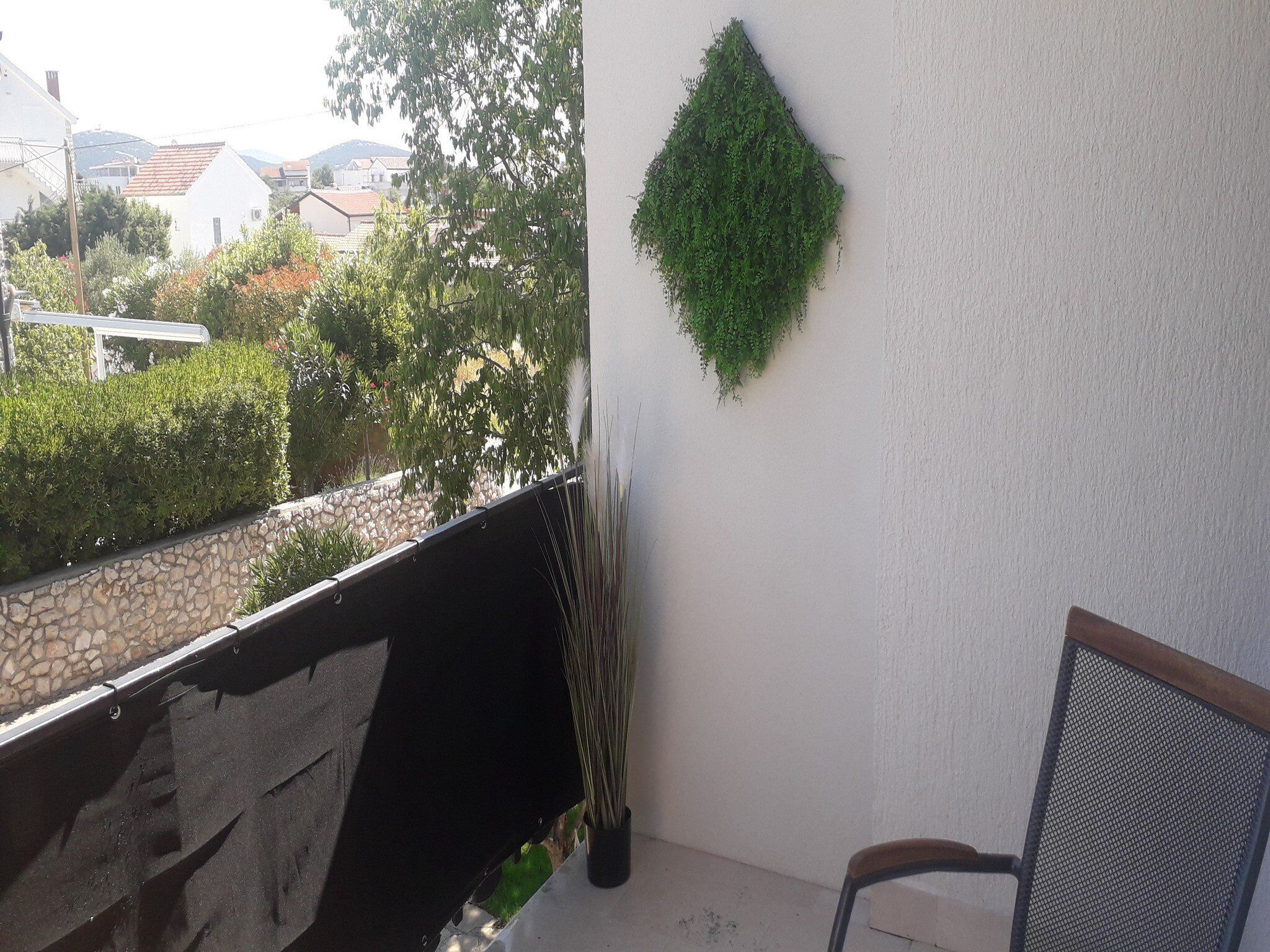 A balcony with a stone wall, a metal chair, and a hanging green plant.