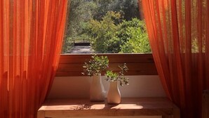 A room with a window framed by red curtains, a wooden bench, and two potted plants. - Elesta 2 Bedroom House (Vourvourou)