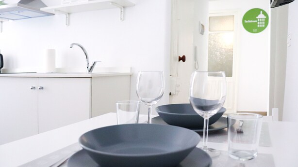 A modern kitchen with white cabinets, a sink, and a countertop. There are two dark bowls and two wine glasses on the table.