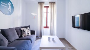 A modern living room with a grey sofa, a white coffee table with two mugs, a floor lamp, and a TV on the wall.
