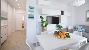 Un espacio de estar moderno con decoración en blanco, que incluye un comedor con una mesa, un frutero, sillas blancas y un sofá.