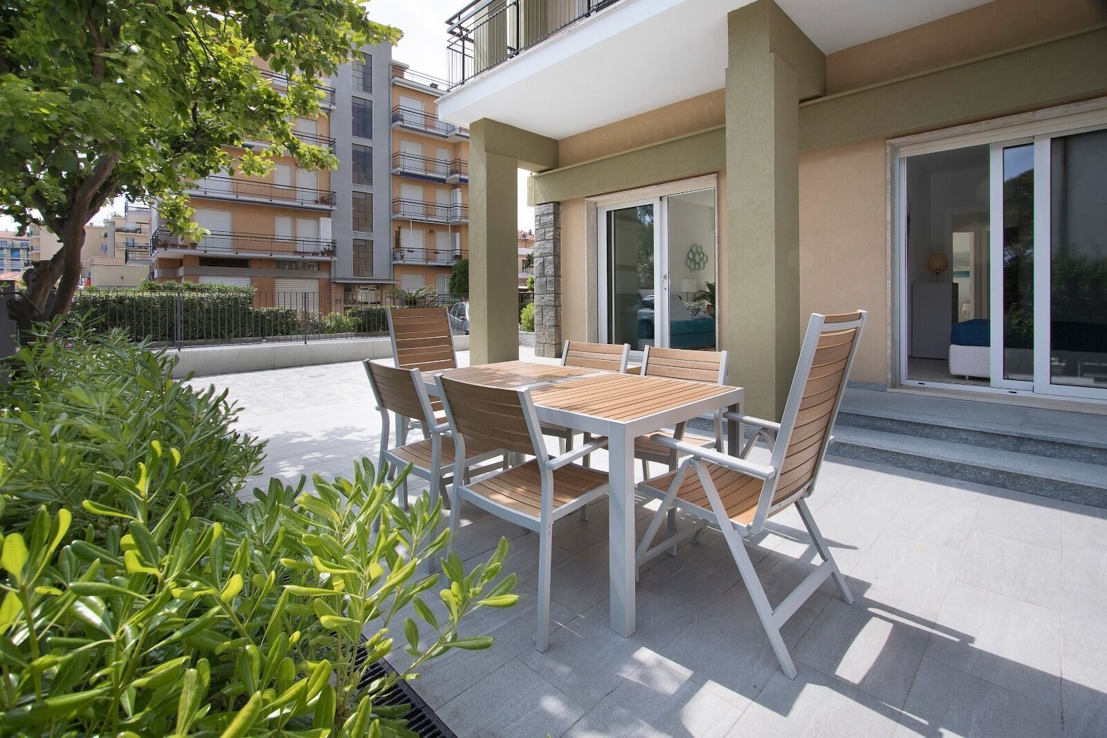 Un patio al aire libre con una mesa y sillas, rodeado de follaje y un edificio con balcones.