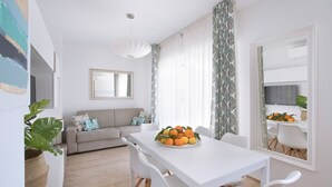 Una sala de estar moderna con un sofá blanco, una mesa de comedor con fruteros y un espejo grande.