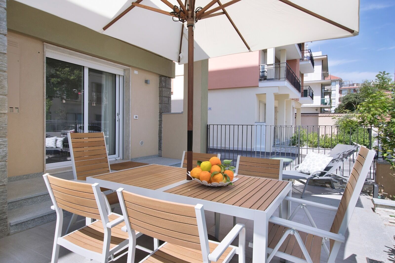 Ein Balkon mit Holztisch und -stühlen, einem großen Sonnenschirm und einer Schüssel Orangen.