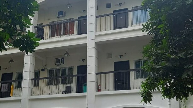 A multi-story building with a tiled roof, balconies, and a parking area with potted plants. - Tesoro Apartments (Manila)