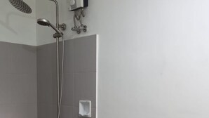 A modern bathroom with a toilet, a shower with a handheld showerhead, and a wall-mounted soap dispenser. - Tesoro Apartments (Manila)