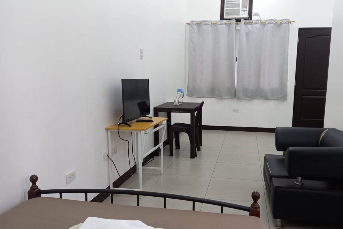 A small, clean room with a bed, a desk with a computer, a chair, and a sofa.