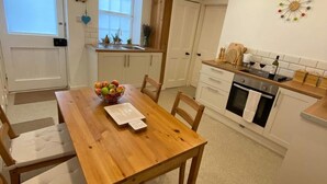 A kitchen with a wooden table, chairs, a fruit bowl, and a clock on the wall. - Newburghaprtment/scotland/sleeps 4/firepit/garden (Cupar)