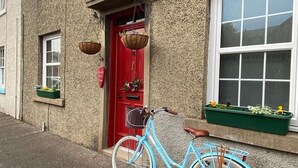 A blue bicycle parked in front of a building with a red door and a window with a green planter. - Newburghaprtment/scotland/sleeps 4/firepit/garden (Cupar)