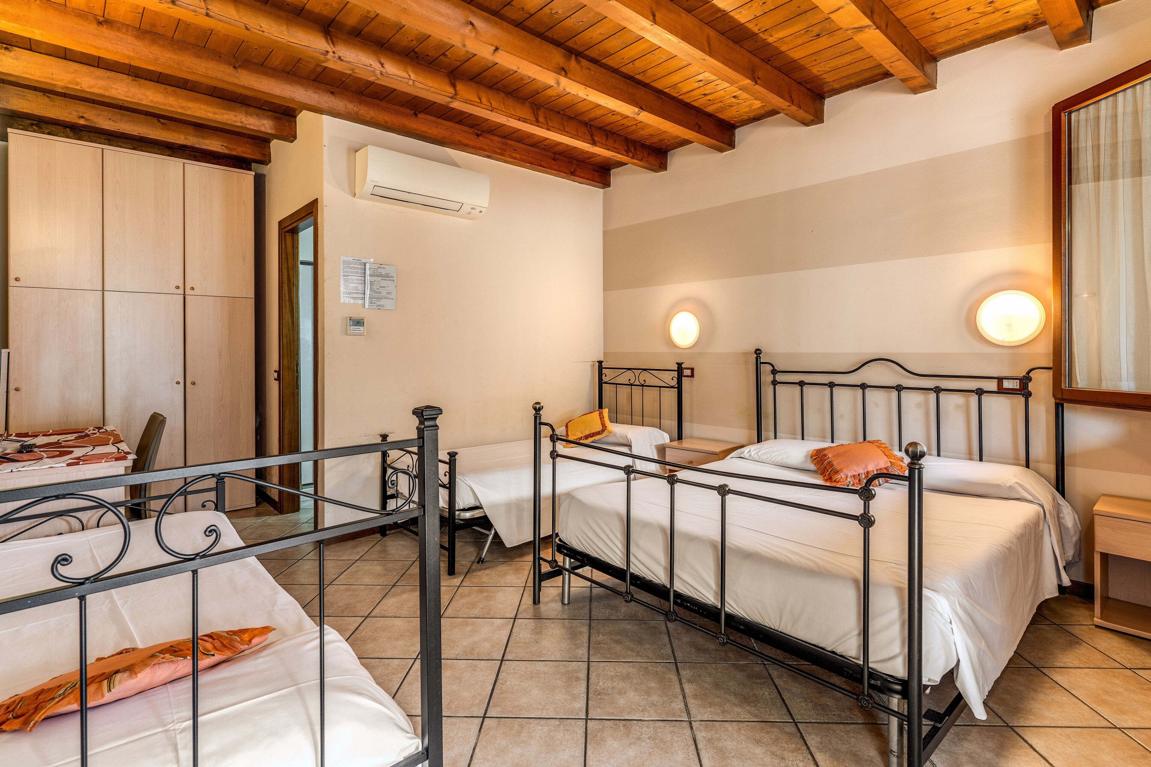 Una habitación con tres camas de metal, vigas de techo de madera y suelo de baldosas.